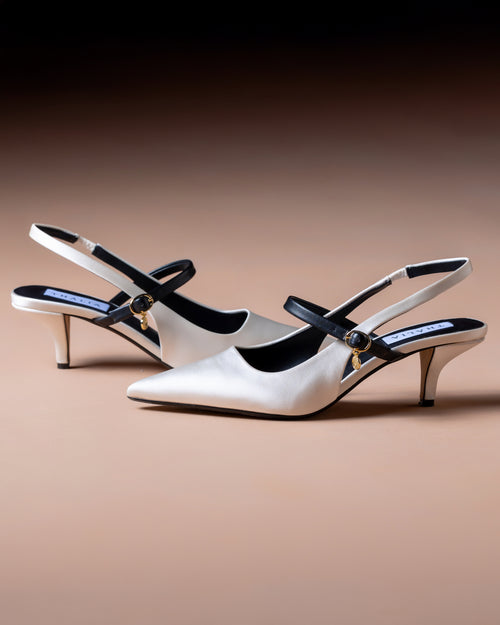 Pair of white high-heeled shoes with black accents on a brown background - made in satin and vegan  sustainable materials by Thalia Dubai