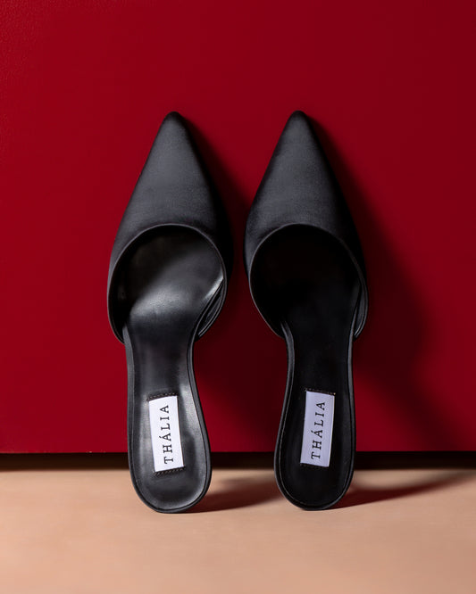 Pair of black pointed-toe shoes with 'Thalia' label on a red and beige background